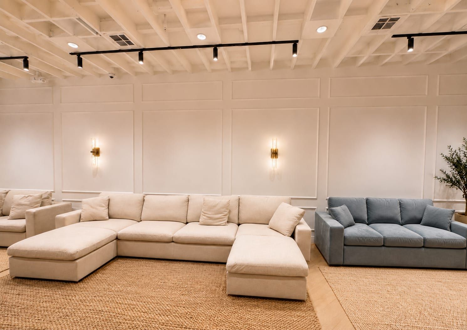 Showroom seating area with cream and blue modular sofas under a coffered ceiling with track lighting and brass wall sconces