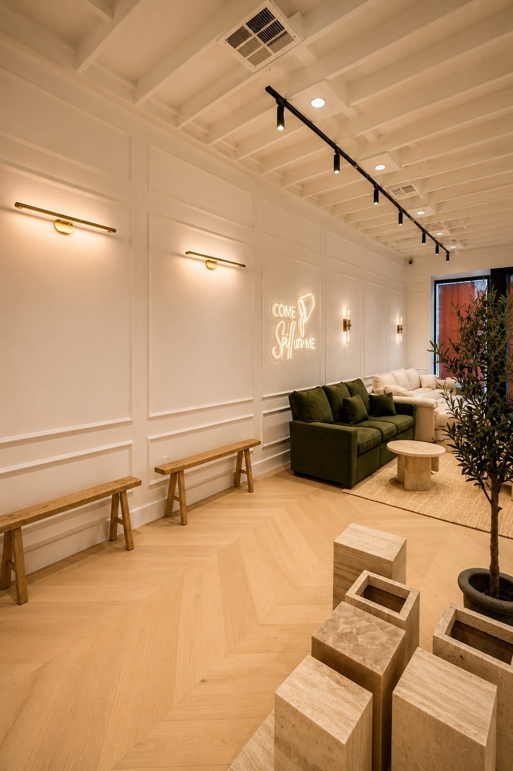 Showroom lounge with neon wall sign, green velvet sofa, travertine display blocks and wooden benches on herringbone flooring