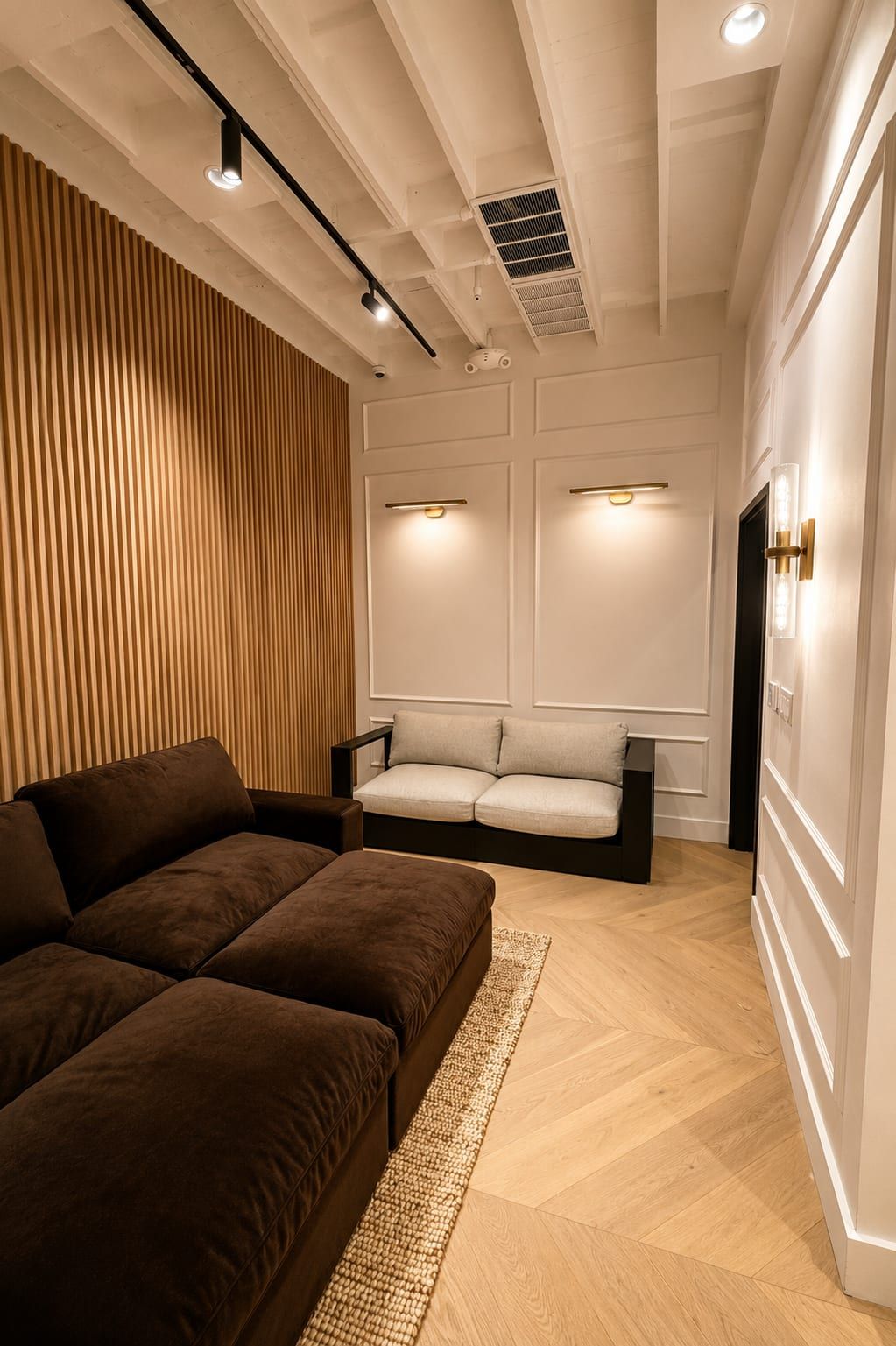 Lounge nook with brown velvet sectional, slat-wood wall, track lighting and brass picture lights over panel moulding