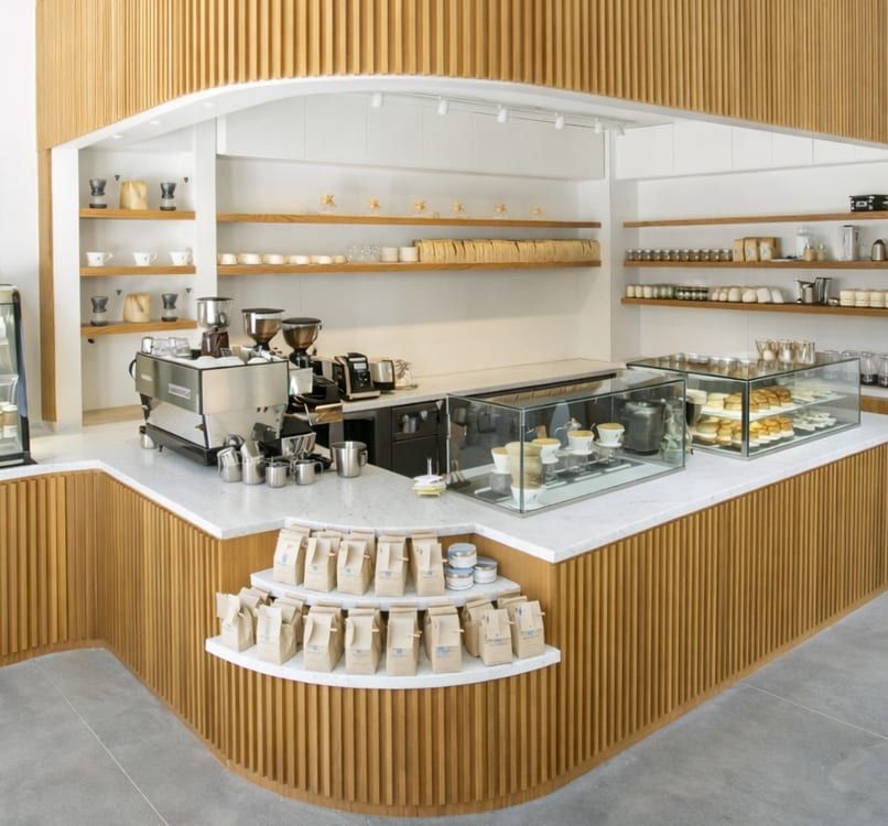 Curved oak soffit arching over the espresso bar, with track lighting, the pastry case and coffee display at the counter's rounded corner